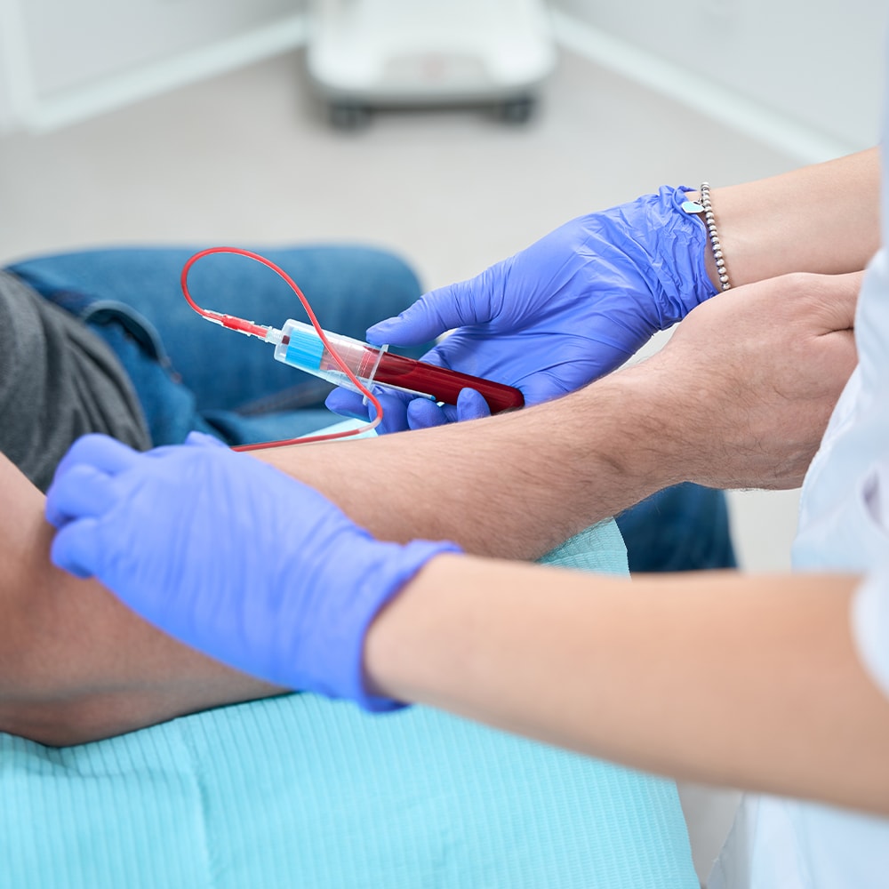 Clinician in blue gloves taking a blood sample from a patient's arm