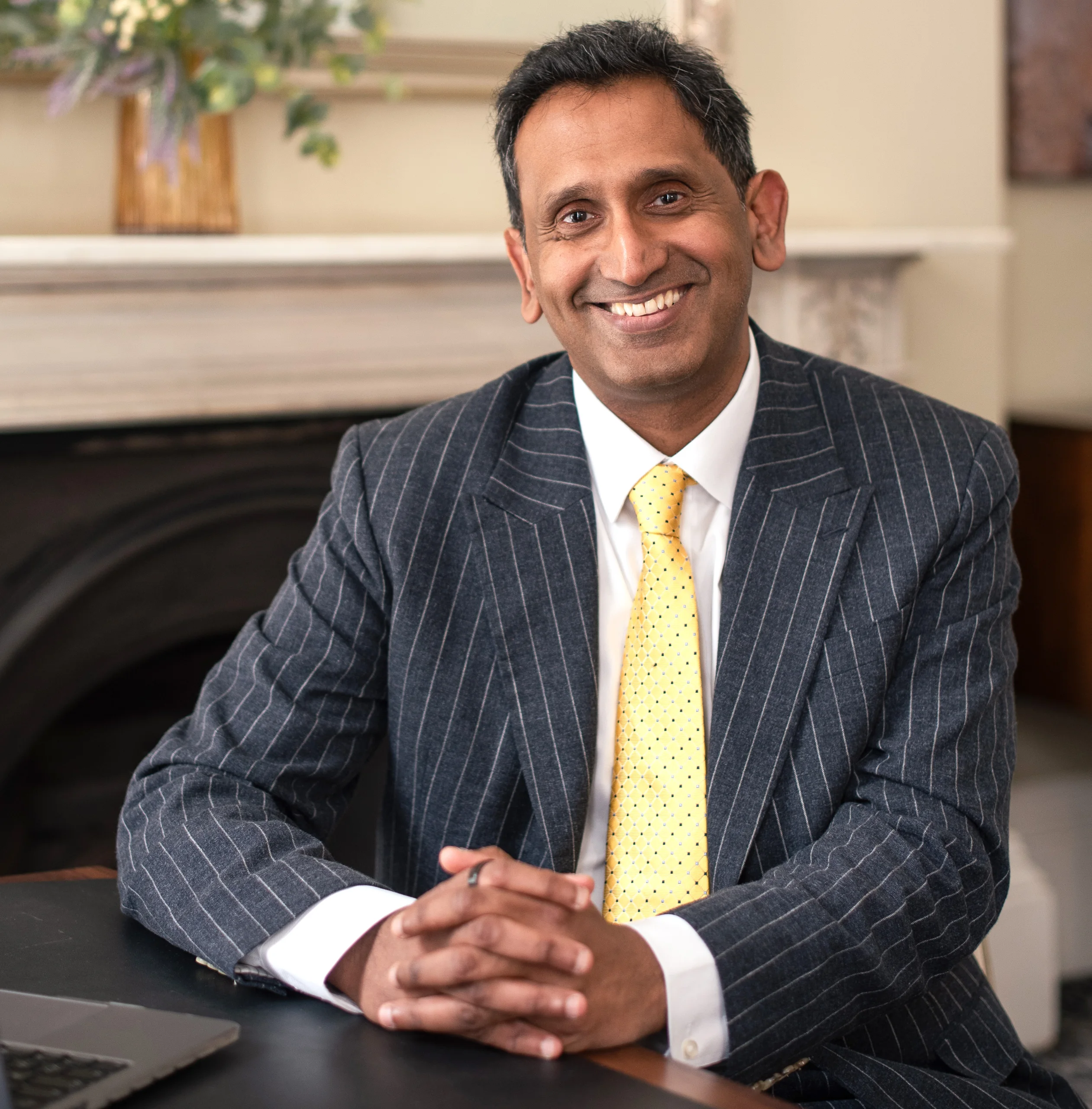 Professor Prasanna Sooriakumaran seated, smiling with hands clasped