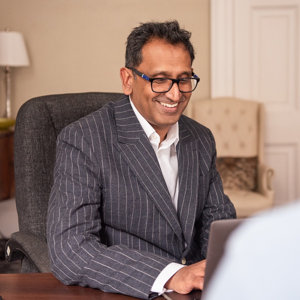 Professor Prasanna Sooriakumaran seated in his clinic, smiling