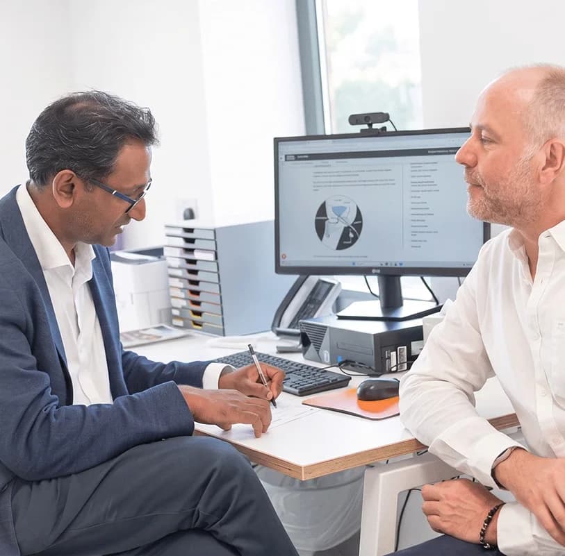 Professor Prasanna Sooriakumaran talking with a patient at his desk